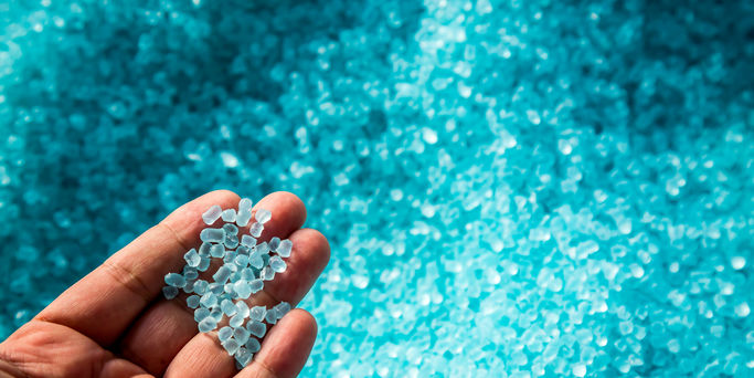 A hand hold or touching plastic pellets , plastic polymer dye granules color clear blue